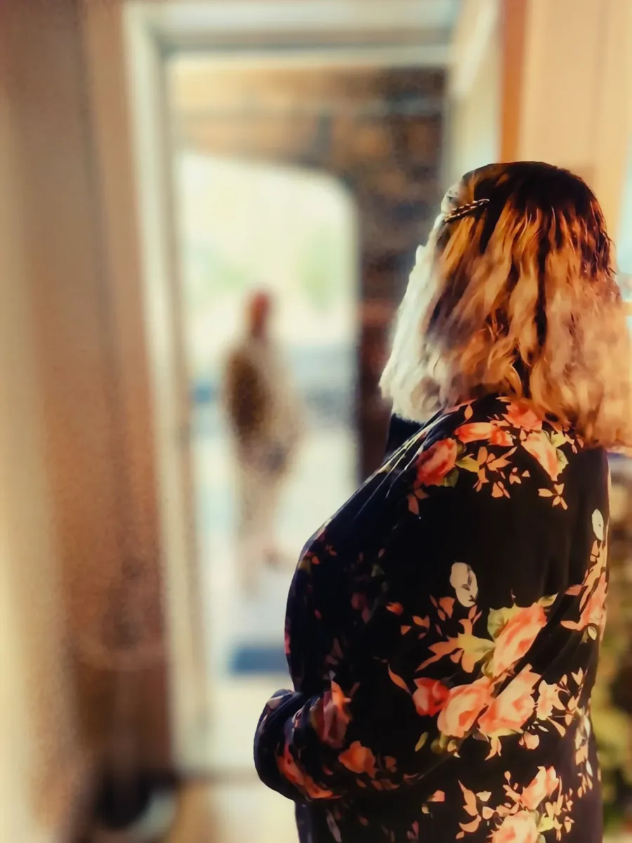 Marianne standing quietly, looking out through an open doorway into the light