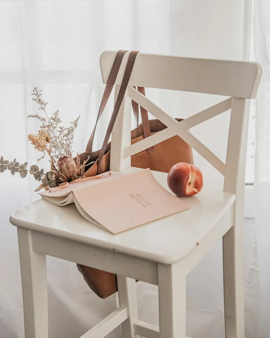 A white chair with an open notebook, dried flowers and a peach